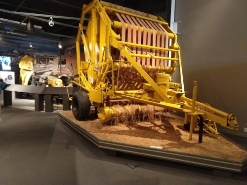A yellow agricultural machine displayed in a museum, with straw and hay visible around it.