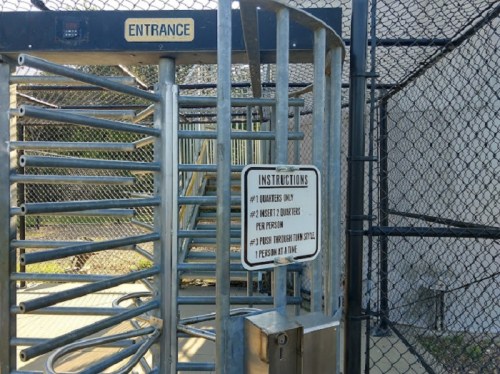 A metal turnstile at an entrance with a sign listing instructions for entry and safety guidelines.