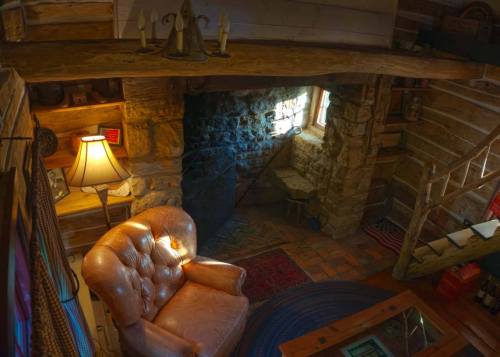 Cozy interior of a rustic cabin featuring a stone fireplace, a plush armchair, and warm lighting.