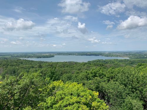 A scenic view of a lake surrounded by lush green trees under a partly cloudy sky.