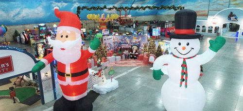 Inflatable Santa and snowman greet visitors in a festive indoor amusement area decorated for the holidays.