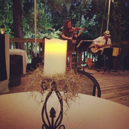 A candle centerpiece on a table with a musician playing guitar and a violinist performing in the background.