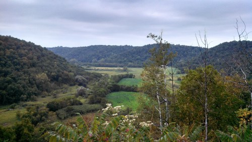 A scenic view of rolling hills and lush green fields under a cloudy sky.