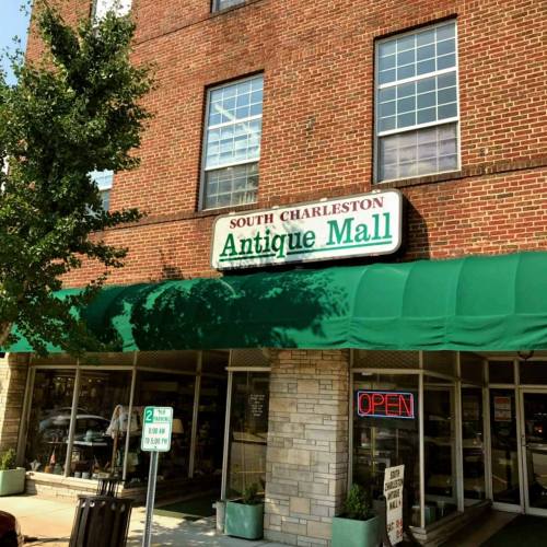 Sign for "Antique Mall" on a brick building with green awning, surrounded by trees and a clear blue sky.