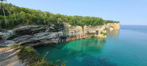 Scenic view of a rocky coastline with lush greenery and clear turquoise water under a blue sky.