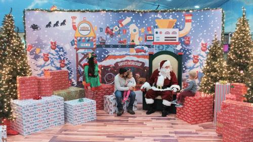 A festive scene with Santa, children, and decorated Christmas trees surrounded by colorful gift boxes.