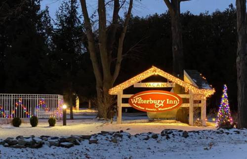Sign for Waterbury Inn, illuminated with holiday lights, surrounded by snow and trees at dusk.