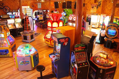 A vibrant arcade filled with various colorful gaming machines and slot machines, featuring wooden decor and bright lights.