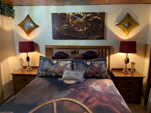 A cozy bedroom featuring a wooden bed with gear-themed bedding, decorative lamps, and wall art.
