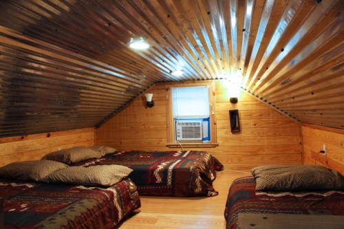 Cozy attic bedroom with wooden walls, two beds, and an air conditioner, featuring a sloped metal ceiling.