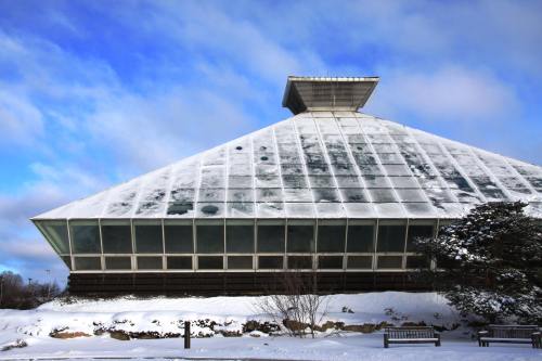 A large, modern glass building with a pyramid shape, surrounded by snow and under a blue sky with clouds.
