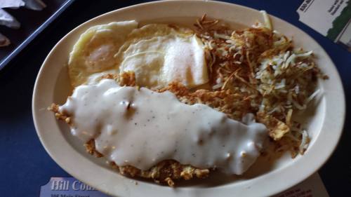 A plate of food featuring two fried eggs, hash browns, and chicken fried steak topped with white gravy.
