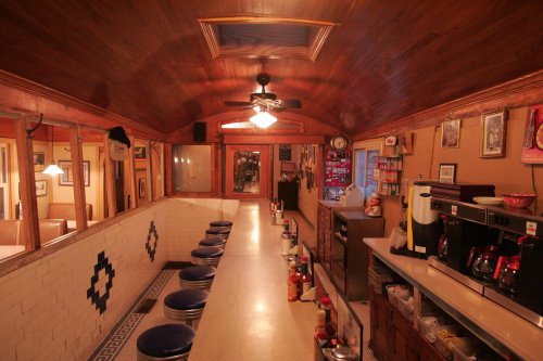 Interior of a vintage diner featuring a long counter with blue stools, wooden ceiling, and nostalgic decor.