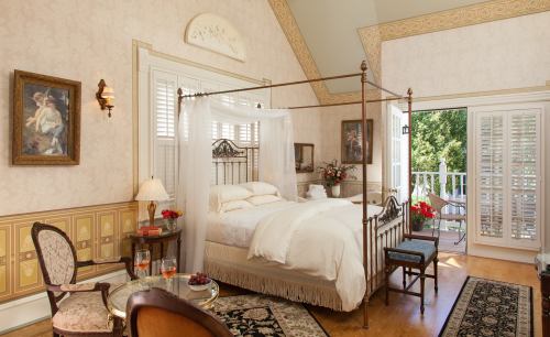 A cozy bedroom with a four-poster bed, elegant decor, and a balcony overlooking greenery.