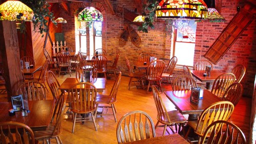 Cozy restaurant interior with wooden tables and chairs, stained glass lamps, and brick walls.