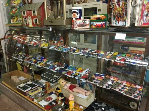 A display case filled with vintage toys, model cars, and collectibles, including a doll and various trinkets.