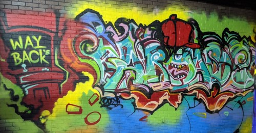Colorful graffiti featuring vibrant designs, text, and a character wearing a red cap on a brick wall.