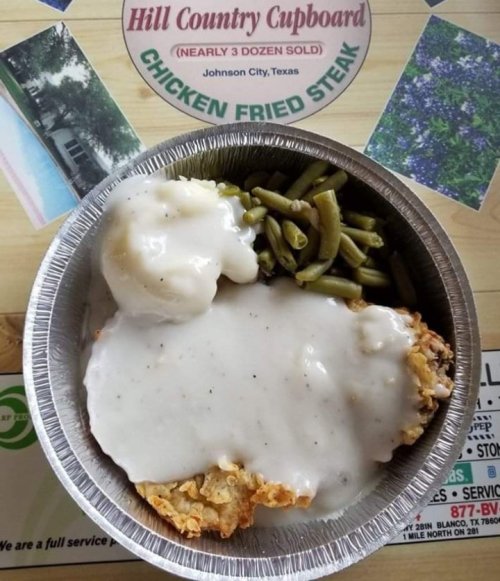 A metal tray with chicken fried steak topped with gravy, green beans, and mashed potatoes on a wooden table.