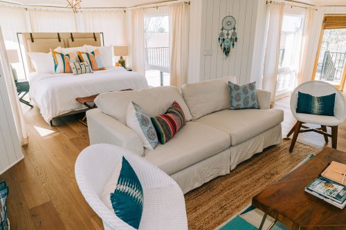 Cozy living space featuring a white sofa, colorful cushions, and a bright bedroom in the background with natural light.