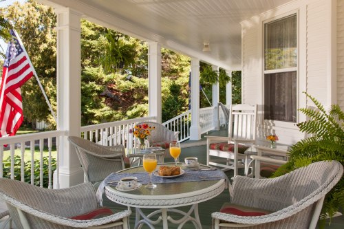 A cozy porch with wicker furniture, a table set with orange juice and pastries, and an American flag in the background.