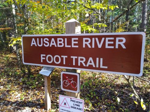 Sign for the Ausable River Foot Trail, featuring a bicycle symbol and a warning about Lyme disease prevention.