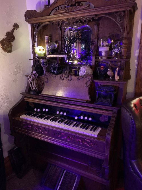 A vintage wooden organ with ornate details, surrounded by decorative items and illuminated with purple light.