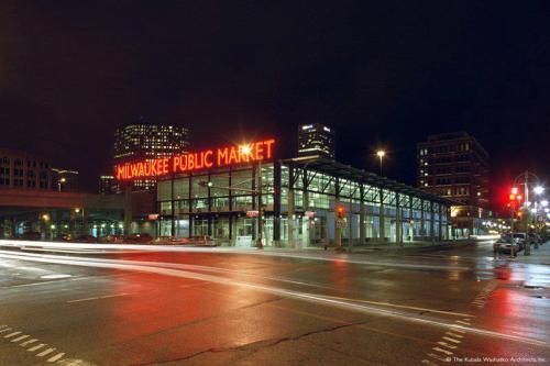 Milwaukee Public Market illuminated at night, with city buildings and traffic lights in the foreground.