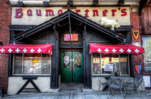 Exterior of Baumortner's restaurant featuring a wooden facade, red awnings, and a decorative cow on the roof.