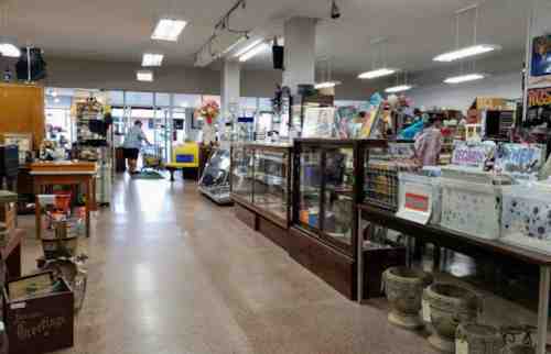 A spacious thrift store aisle with display cases, shelves of items, and bright overhead lights.