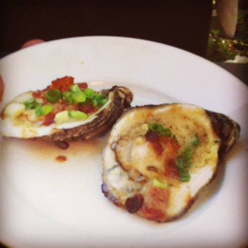 A plate with two baked oysters topped with green onions and bacon bits.