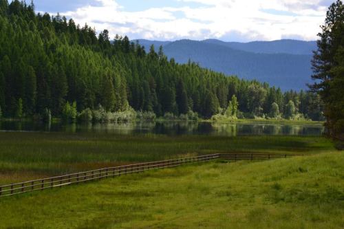 A serene landscape featuring a calm lake surrounded by lush green trees and distant mountains under a partly cloudy sky.