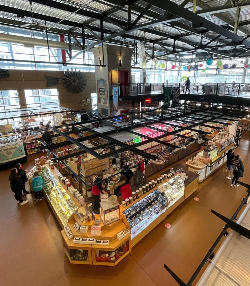 Aerial view of a bustling market with various stalls, shoppers, and colorful decorations in a spacious, well-lit area.