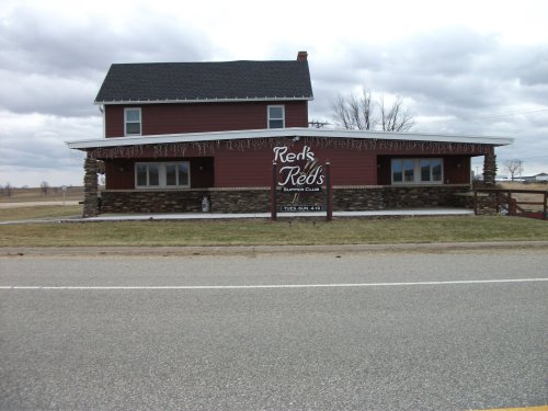 A red two-story building with stone accents and a sign reading "Red's Supper Club," set against a cloudy sky.