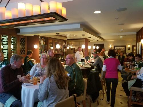A lively restaurant scene with diners enjoying meals and drinks, some wearing sports jerseys, in a cozy atmosphere.