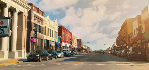 A charming downtown street lined with historic buildings, shops, and parked cars under a bright sky.