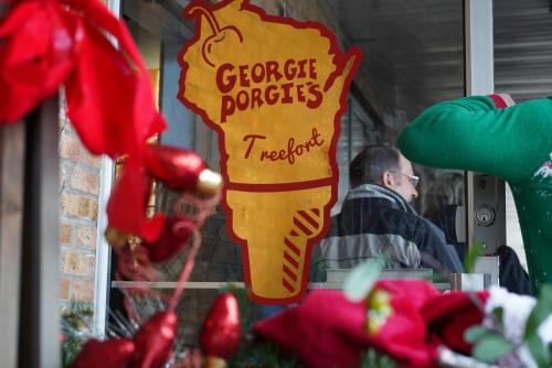 A festive storefront with a sign reading "Georgie Porgie's Treefort," decorated with holiday ornaments and greenery.