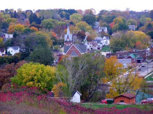 A scenic view of a small town with colorful autumn trees, featuring a church steeple and residential buildings.