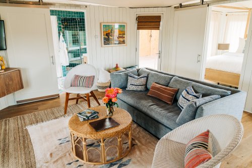 Cozy living area with a gray sofa, woven coffee table, and colorful decor, featuring natural light and a warm atmosphere.