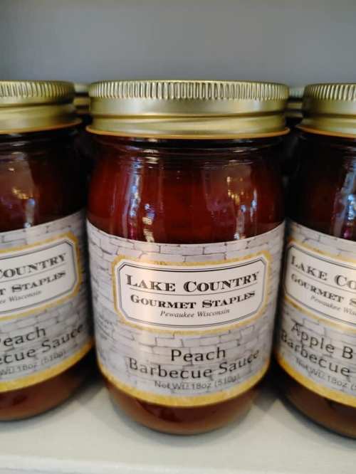 Three jars of Lake Country Gourmet Staples barbecue sauce, labeled "Peach" and "Apple," on a shelf.