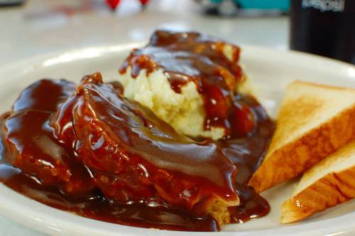 A plate of meatloaf covered in brown gravy, served with mashed potatoes and toast.