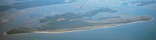 Aerial view of a large, elongated island surrounded by water, with lush greenery and sandy shores.