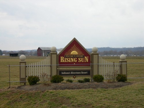 Sign welcoming visitors to Rising Sun, Indiana, featuring a sun design and information about the Riverton Resort.