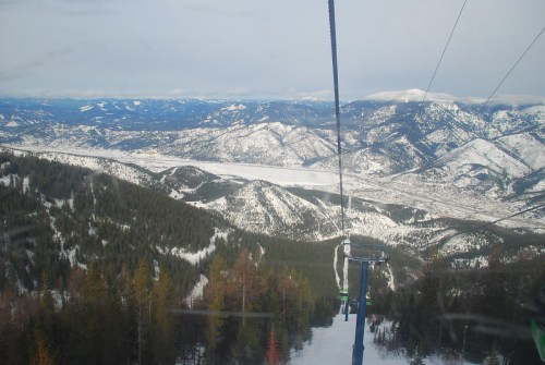 A scenic view from a ski lift, overlooking snow-covered mountains and a valley below.