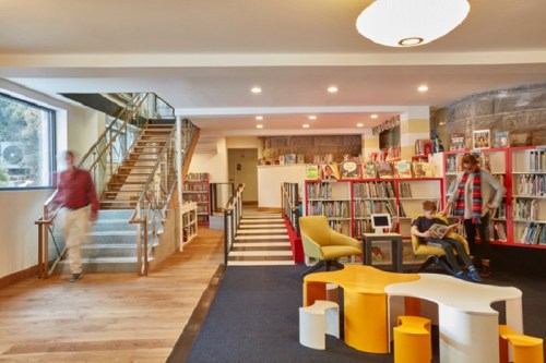 A modern library interior with colorful furniture, bookshelves, and people reading and walking.
