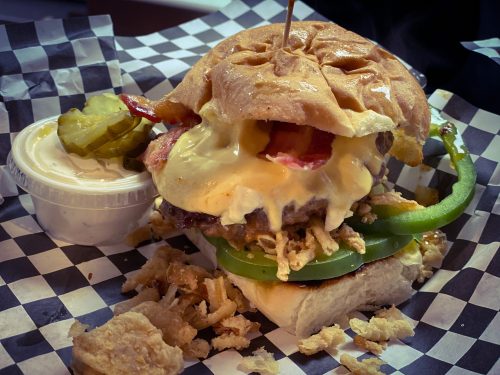A juicy burger with melted cheese, bacon, and green peppers, served with pickles and a side of ranch dressing.
