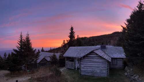 A rustic cabin surrounded by trees under a colorful sunset sky.