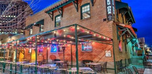 A brick restaurant exterior with outdoor seating, adorned with colorful lights, set against a twilight sky.