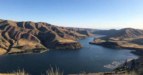 A scenic view of a river winding through mountains, with boats docked along the shore under a clear blue sky.