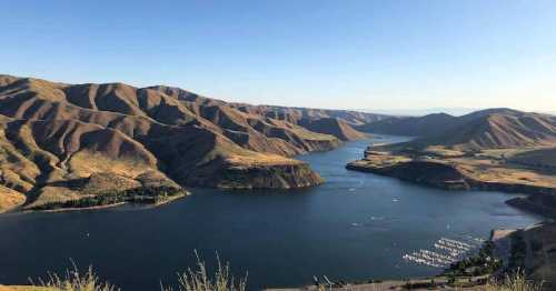 A scenic view of a river winding through mountains, with boats docked along the shore under a clear blue sky.