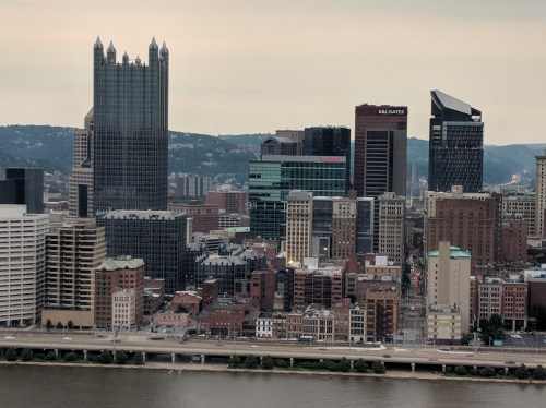 Aerial view of Pittsburgh's skyline featuring tall buildings along the river under a cloudy sky.